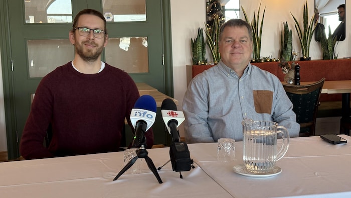 Deux hommes sont assis à une table avec des micros.