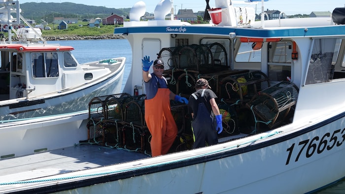 Un pêcheur sur un bateau rempli de cage fait un signe de la main.