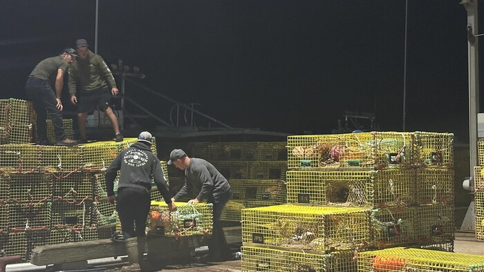 Des travailleurs embarquent des casiers à homard sur un bateau.