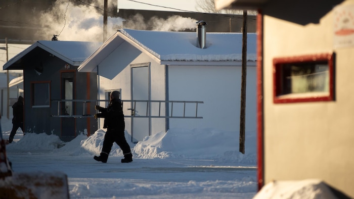 Un homme qui transporte une échelle devant les cabanes de pêche.
