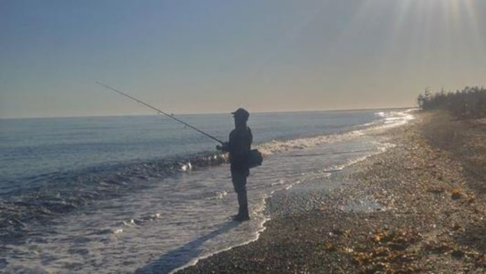 Un pêcheur sportif debout sur le rivage, avec sa canne à pêche