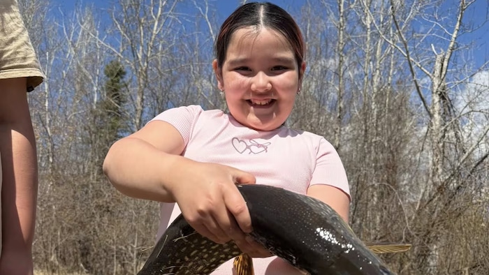 Une petite fille toute souriante tient un poisson. 