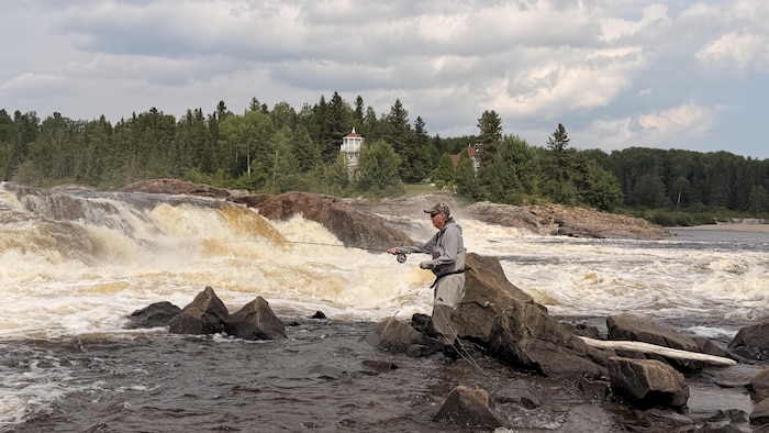 Un homme pêche à la mouche dans une rivière.