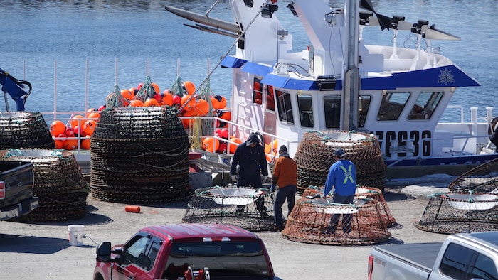 Des travailleurs sur le quai manipulent des équipements de pêche. En arrière-plan : un bateau.