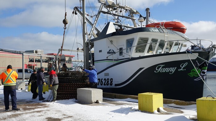 Un bateau de pêche est à quai, des hommes installent des paniers de pêche à crabe à une grue.