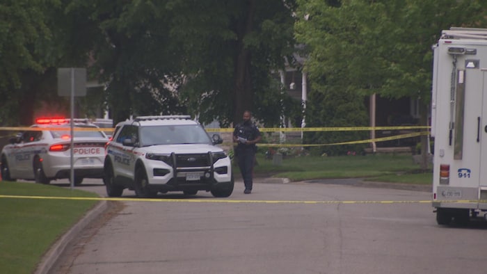 Un policier traverse la rue, où sont stationnés des véhicules de police et le camion médico-légal de la police régionale de Durham, le 29 mai 2025.