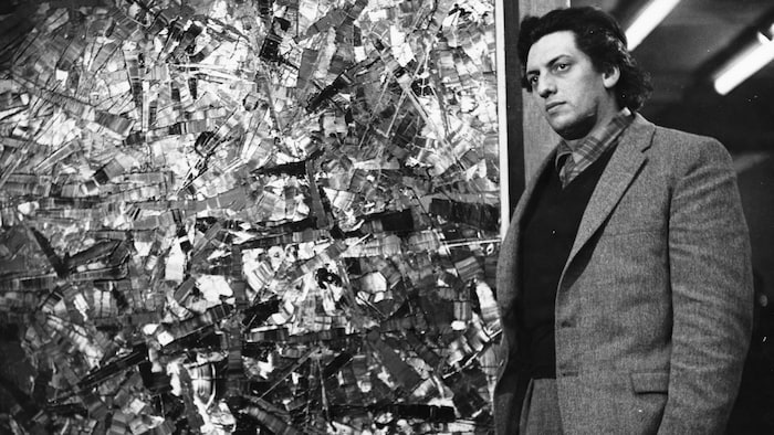 Le peintre québécois Jean-Paul Riopelle debout, près d'une de ses toiles.