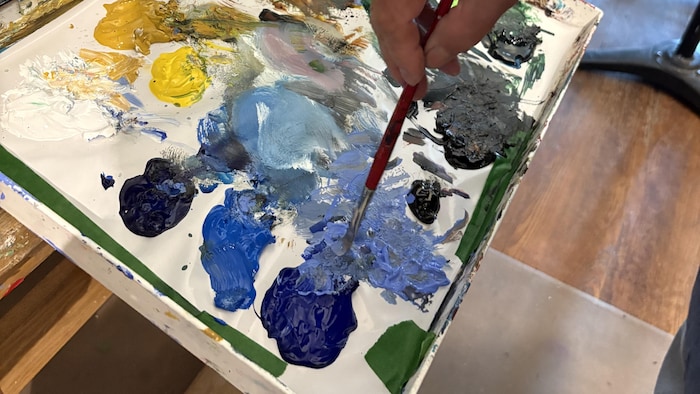 La tablette du chevalet en gros plan. Plusieurs couleurs de peinture y sont réparties.
