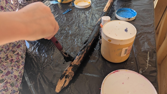 Des petites mains peinturent un bout de bois.