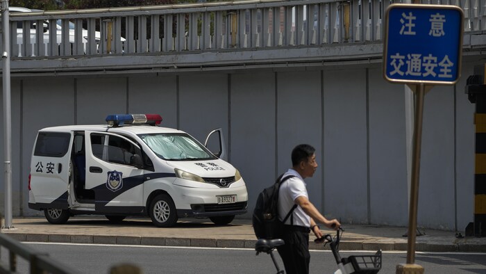 一名男子推着自行车，从警车旁经过。