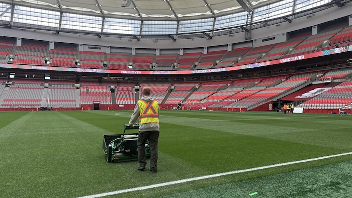Un travailleur pousse une tondeuse sur une pelouse fraîchement tondue à l'intérieur du stade.