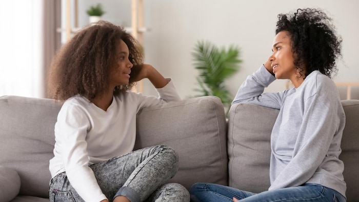 Une adolescente et sa mère discutent assises sur un canapé.