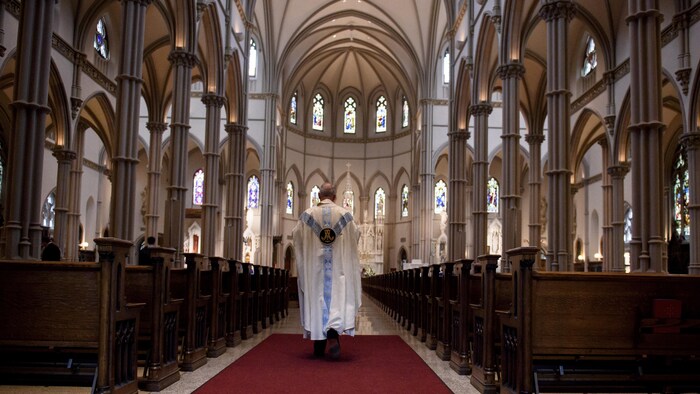 Un prêtre marche dans l'allée centrale d'une église.