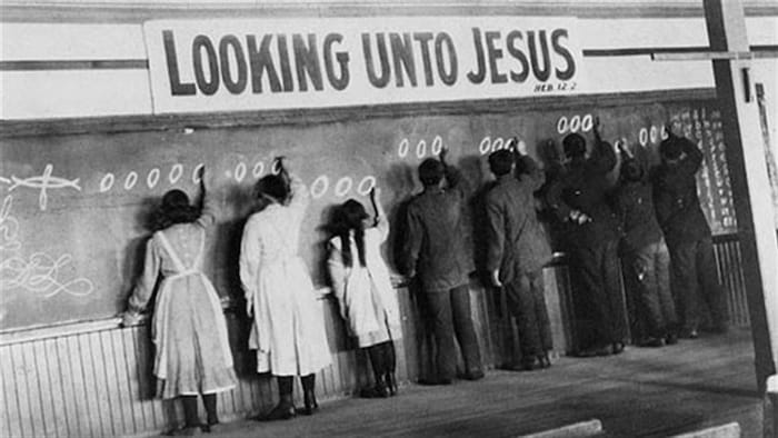 Des enfants autochtones écrivent le chiffre zéro au tableau d'une classe au-dessus duquel est écrit le verset biblique «Fixant nos yeux sur Jésus».