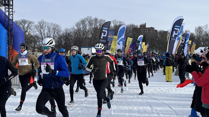 Des dizaines de coureurs partent sur la neige, encouragés par des dizaines de personnes installées près de la piste enneigée. 