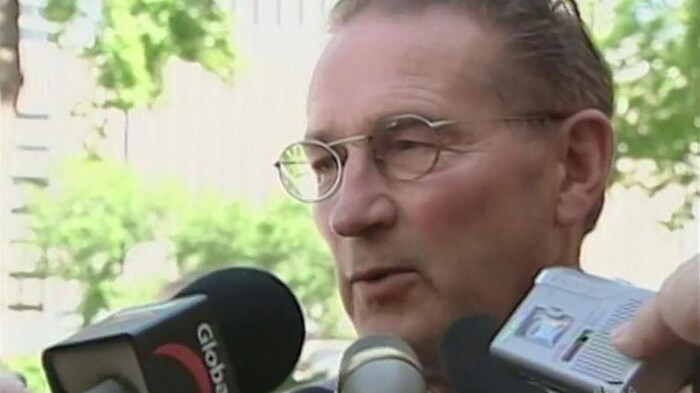 Gros plan sur le visage de Percy Schmeiser entouré par des micros de journalistes.
