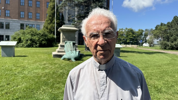 Le père Emery Brien pose pour la photo devant la statue du père Camille Lefebvre renversée.