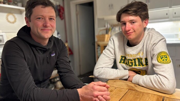 Un père et son fils souriants tous les deux sont assis l'un à côté de l'autre autour d'une table dans une maison.