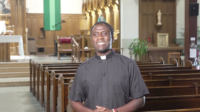 Le père Gustave Ineza debout, souriant, dans une église.
