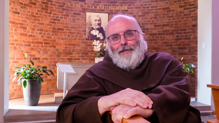 Un homme sourit légèrement à la caméra. 