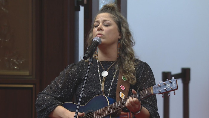 Una mujer canta ante el micrófono con una guitarra.