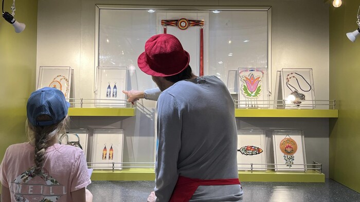 Un animateur du musée ambulant pointe du doigt une œuvre en perle, une enfant regarde.