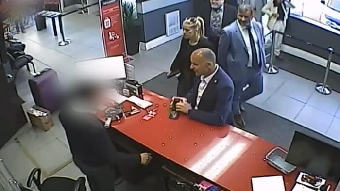 Image tirée d'une caméra de surveillance où un enquêteur montre son insigne derrière un comptoir.