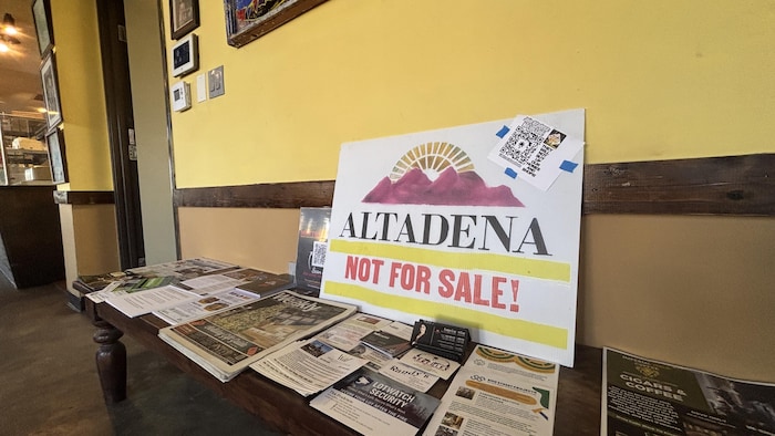 Une affiche en anglais indiquant qu'Altadena n'est pas à vendre posée sur une table contre le mur. 