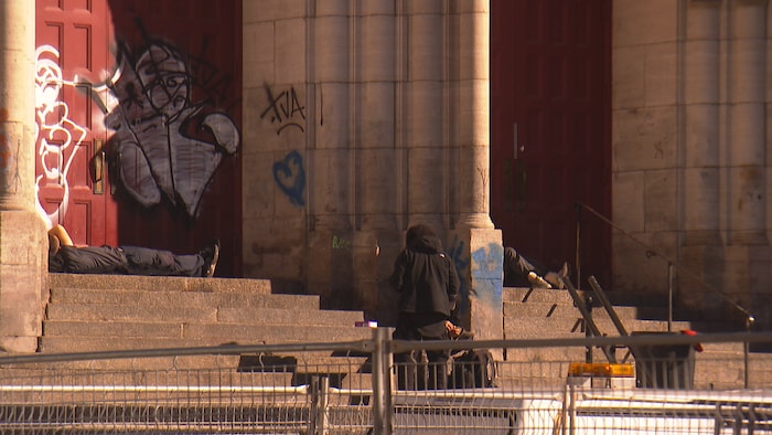 Des personnes en situation d'itinérance se prélassent sur un parvis d'église. 