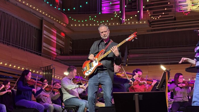 L'homme joue de la basse sur scène devant un orchestre.