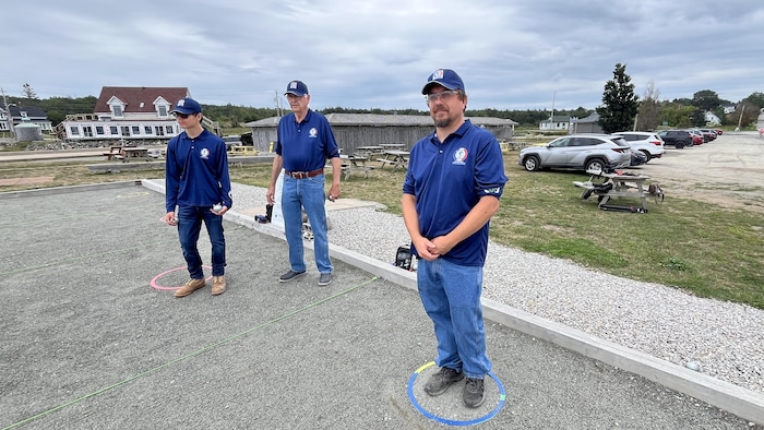Trois hommes jouent à la pétanque sur un boulodrome.