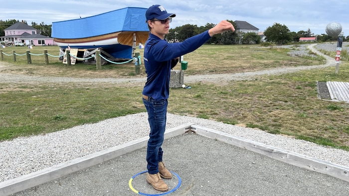 Un jeune joueur de pétanque lance une boule dans un boulodrome.