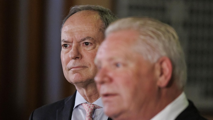 Peter Bethlenfalvy regarde à l'horizon lors d'un point de presse à côté de Doug Ford. 
