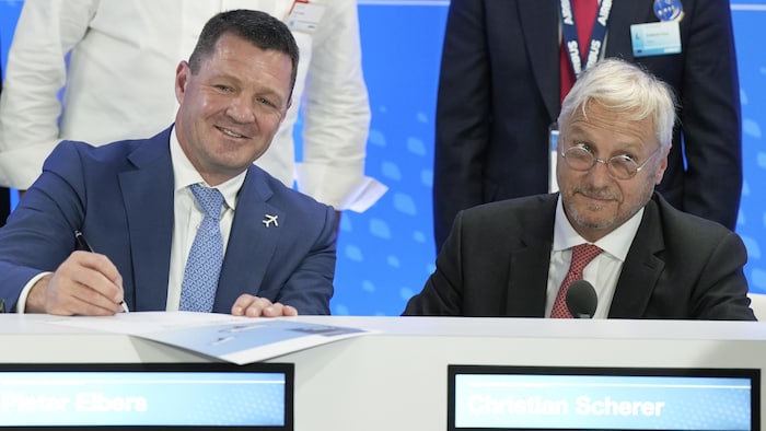 Deux hommes sourient en signant un document.