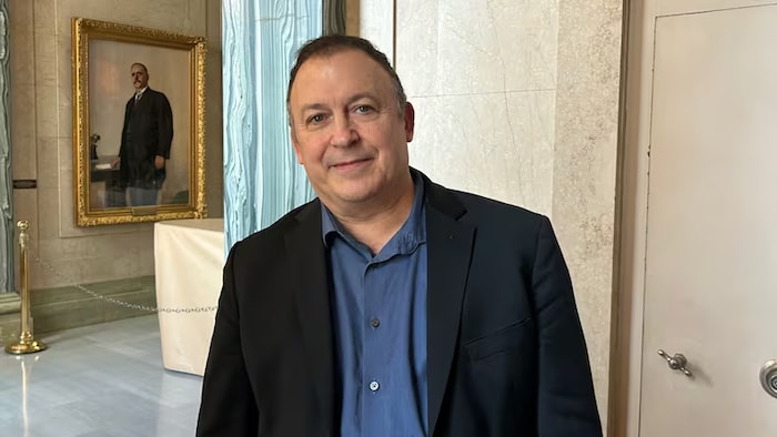 Peter Gilmer est debout dans une salle et on le voit dans un miroir au fond.