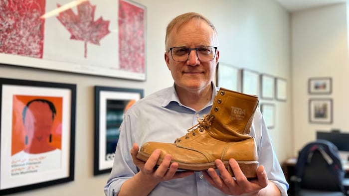Peter Julian tient une botte de travailleur dans ses mains.