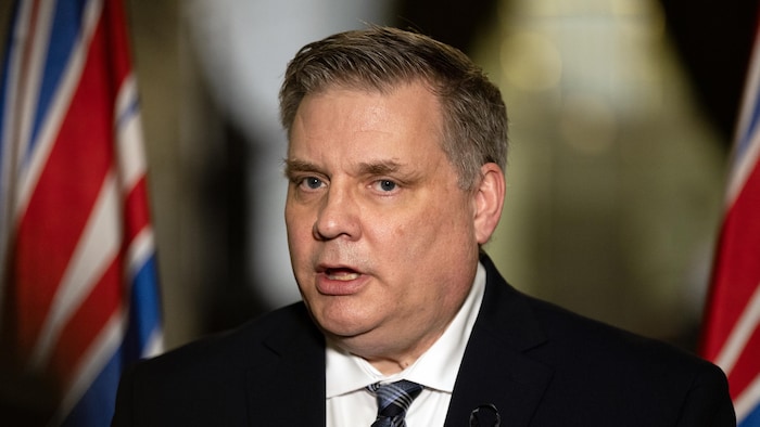 Peter Milobar est devant des drapeaux.