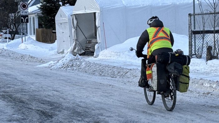 Un cycliste de dos en pleine saison hivernal qui porte plusieurs sacoches sur son vélo avec une veste colorée et un casque de vélo.
