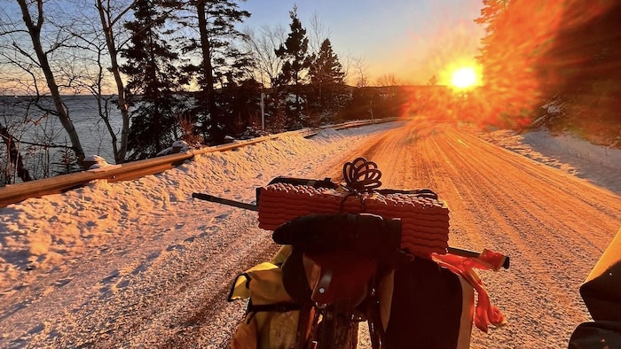 Le vélo de Petit Donnie, sur une route enneigée, lors d'un coucher de soleil.