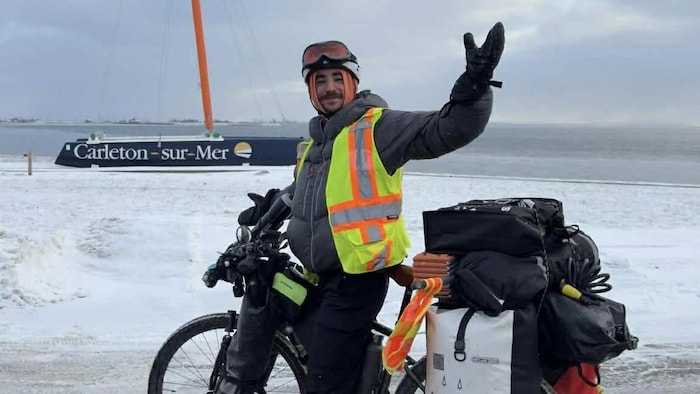 Donnie Edery est un jeune cycliste habillé chaudement, sur son vélo, en hiver. Il pose devant l'écriture de Carleton-sur-Mer.