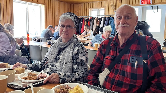 Henriette et Gérald, attablés dans une salle chaleureuse devant un repas traditionnel de cabane à sucre.
