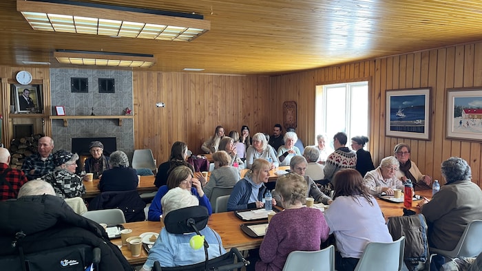 Des personnes aînées assises autour de longues tables dans une salle chaleureuse.