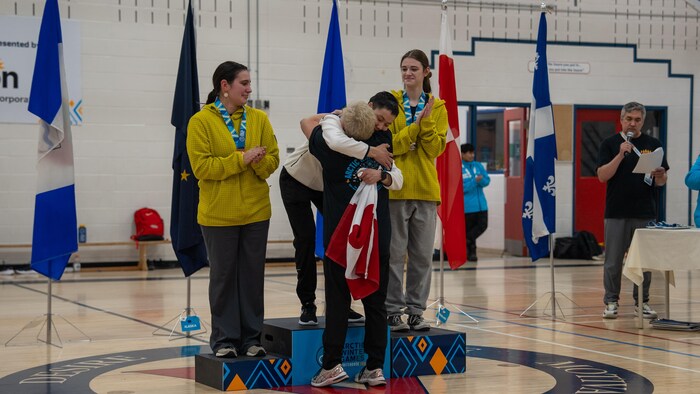 Une athlète sur un podium enlace une femme en tenant un drapeau.