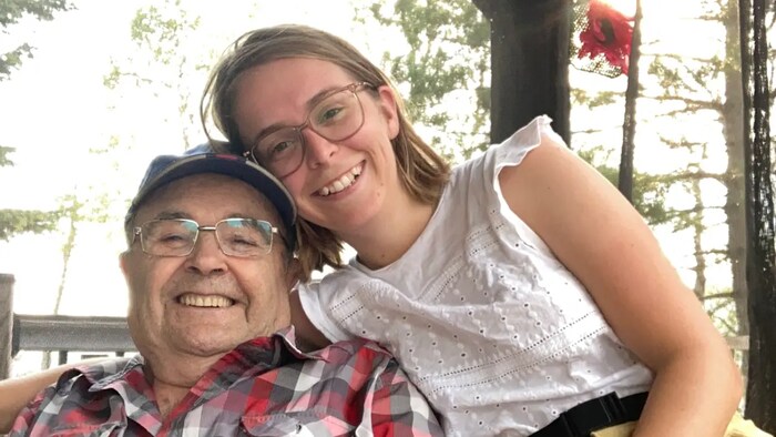 une jeune fille assise avec son grand-père. Ils ont tous les deux un visage souriant.