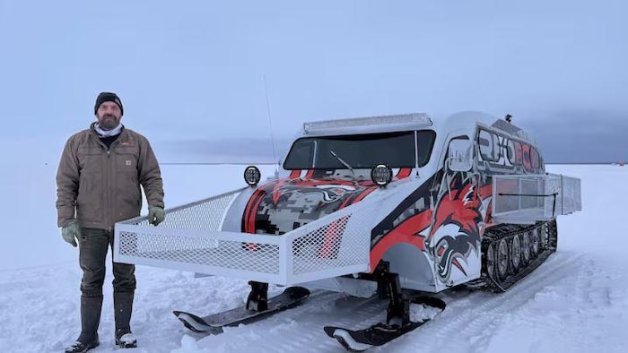 Un homme debout dans la neige à côté d'une machine à chenilles.