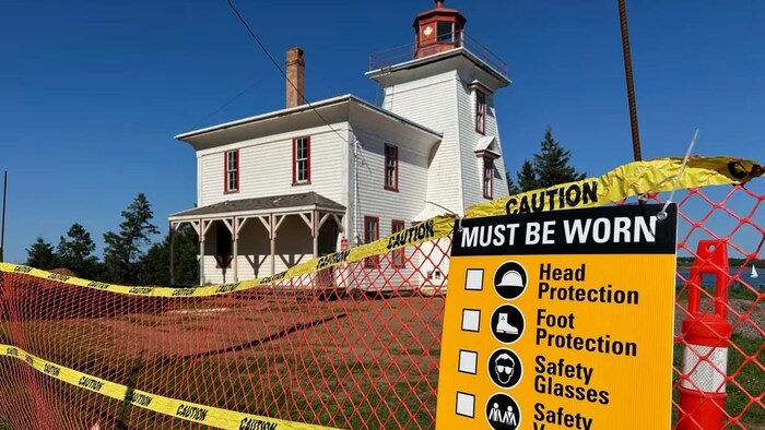 Une clôture et une affiche expliquant les règles de sécurité sur un chantier devant le phare.