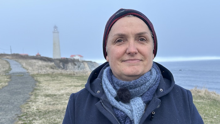 Elle regarde devant et le phare de Cap-des-Rosiers est au loin derrière elle.