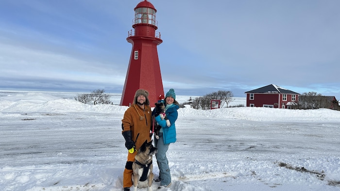 Un couple avec deux chiens se tient en hiver, devant le phare de La Martre.