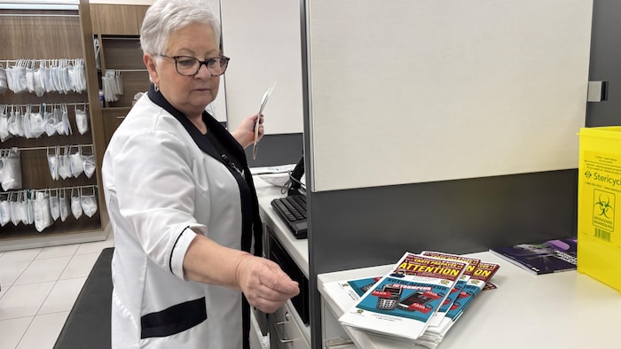 Une employée de pharmacie pige dans une pile de dépliants de sensibilisation sur la fraude. 