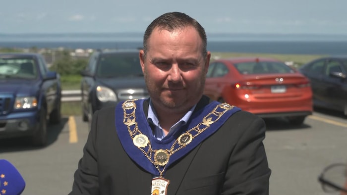 Un homme en entrevue avec un colier sur lequel on peut y lire la Ville de Wabana.